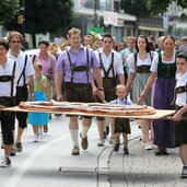 zwei starke maenner tragen die grosse brezn zum breznsuppnest